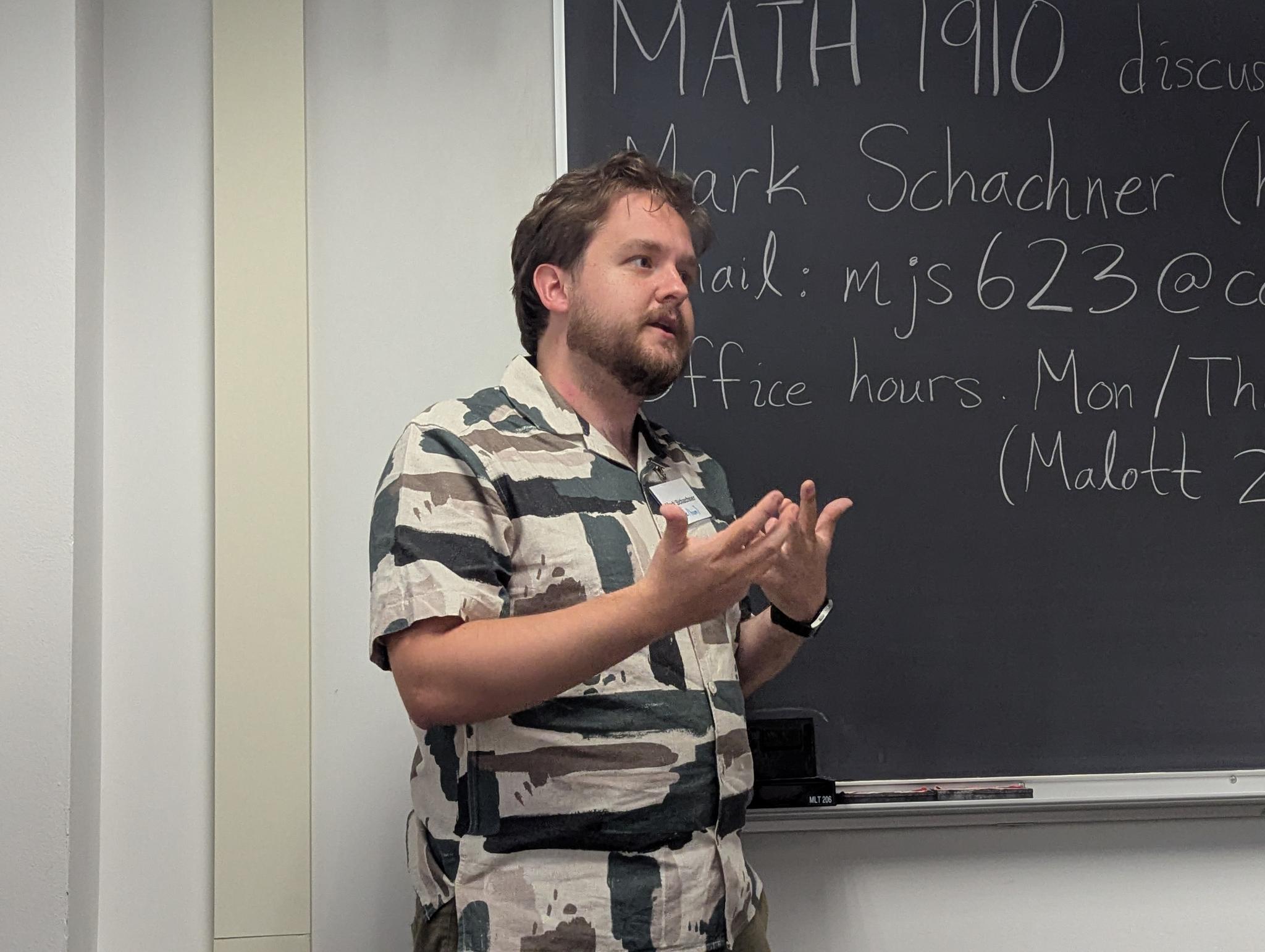Mark Schachner speaking in front of a blackboard while teaching MATH 1910